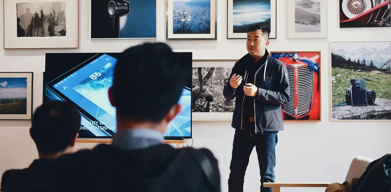 A Man Presenting To An Audience, Gesturing As He Explains His Topic In A Well Lit Conference Room A Man Presenting To An Audience, Gesturing As He Explains His Topic In A Well Lit Conference Room