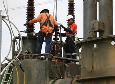 Two technicians working on a transformer inside a power plant, engaged in electrical maintenance
